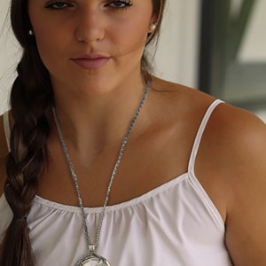 May include: A woman wearing a white tank top and a straw cowboy hat with a black band. She is wearing a silver necklace with a horse head pendant.