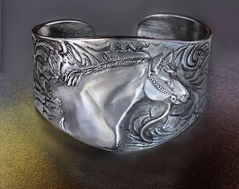 May include: A silver bracelet with an embossed design of a horse's head. The horse is wearing a bridle and has a detailed mane and tail.
