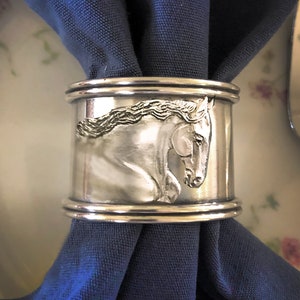 May include: Silver napkin ring with a detailed engraved image of a horse's head.