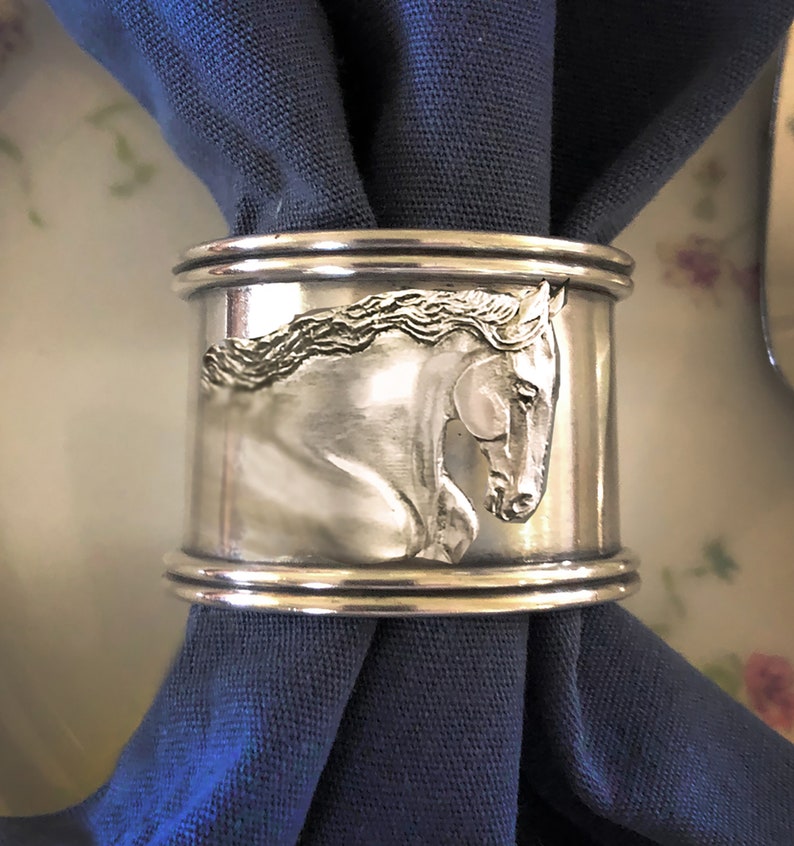 May include: Silver napkin ring with a detailed engraved image of a horse's head.