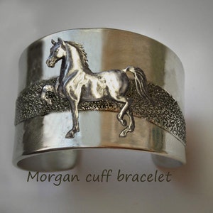 May include: Silver cuff bracelet with a raised image of a horse. The bracelet has a textured band.