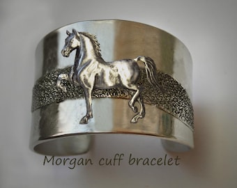 May include: Silver cuff bracelet with a raised image of a horse. The bracelet has a textured band.