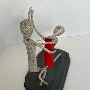 Pu&ograve; includere: Una scultura in cartapesta di una coppia che balla. L'uomo indossa una camicia bianca e la donna un vestito rosso. La scultura &egrave; su una base nera.