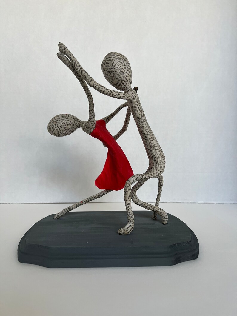 Pu&ograve; includere: Una scultura in cartapesta di una coppia che balla. L'uomo tiene la mano della donna e entrambi sorridono. La scultura &egrave; dipinta in tonalit&agrave; di grigio e rosso.