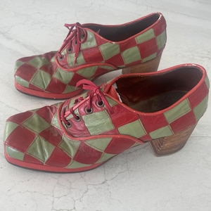 May include: A pair of vintage-style shoes with a red and green checkerboard pattern. The shoes have a square toe, red laces, and a wooden block heel. The shoes are made of leather and have a unique, retro design.