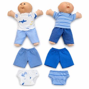 May include: Two Cabbage Patch Kids dolls with various outfits. One doll wears a white shirt with blue shark graphics and blue pants. The other doll wears a blue striped shirt and blue pants. Additional blue shorts and underwear are also included.