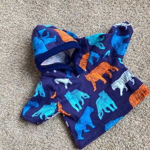 May include: A dark purple hooded sweatshirt featuring a repeating pattern of tigers in bright orange, light blue, and white. The garment has short sleeves, a hood with a dark blue ribbed trim, and a straight hemline across the bottom.