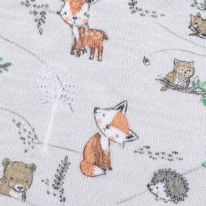 May include: A close-up of a white fabric featuring a repeating pattern of woodland creatures. The design includes a fox, deer, owl, squirrel, bear, and hedgehog, all in a cartoon style. Green leaves and grey lines complete the forest scene.