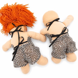 May include: Two dolls viewed from the back, both wearing leopard print shorts with black ribbon ties. One doll has bright orange yarn hair, while the other is bald. Both dolls have light beige skin tones and are positioned against a plain white background.
