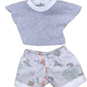 May include: A gray doll outfit featuring a short-sleeved top and shorts. The top has a white collar, and the shorts are patterned with woodland creatures like foxes and hedgehogs. The outfit is designed for a doll.