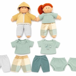 May include: Two dolls with soft features, one wearing a yellow hooded jacket and light gray pants, the other with red yarn hair in a green top and plaid pants. Included are extra outfits: two shirts, one pair of light gray pants, one pair of plaid shorts, one pair of dark green shorts, and two pairs of green briefs.