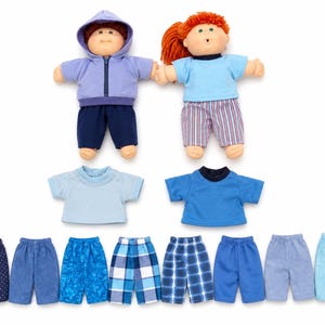 May include: Two dolls with yarn hair, one wearing a lavender hoodie and navy pants, the other in a light blue shirt and striped pants. Included are two extra t-shirts and eight pairs of pants in various shades of blue with patterns like plaid, dots, and tie-dye.