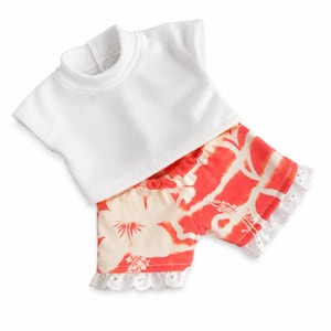 May include: A doll outfit consisting of a plain white short-sleeved shirt with a mock neck and a pair of coral-coloured shorts featuring a cream-coloured floral pattern and white eyelet lace trim along the bottom edges of the legs.