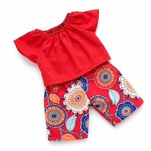 May include: A two-piece outfit consisting of a solid red short-sleeved top with a gathered elastic neckline and a pair of red shorts featuring a repeating floral pattern in shades of orange, dark blue, and light blue with white accents.