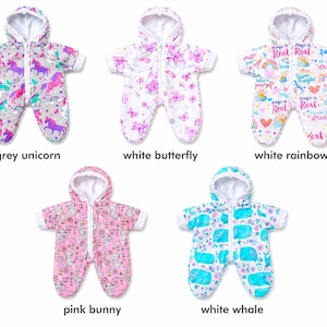 May include: Five hooded doll jumpsuits with front zippers and white linings. Patterns include grey with unicorns, white with butterflies, white with rainbows and text reading magic is real, pink with bunnies, and white with blue whales and flowers.