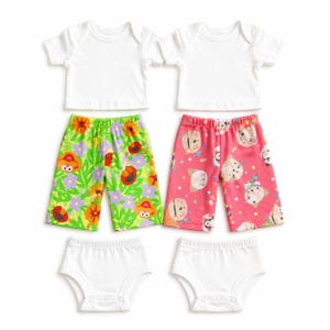 May include: Two sets of baby clothing. Each set includes a white t-shirt, patterned shorts, and a white nappy cover. The shorts feature colorful Sesame Street character designs on a green floral background and a pink background.