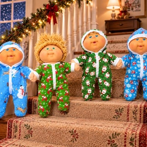 May include: Four dolls with round faces and yarn hair wearing hooded zip-up jumpsuits. The first doll wears a blue jumpsuit with snowman prints, the second has yellow yarn hair and a green jumpsuit, the third wears a green Santa print, and the fourth a blue snowflake print.