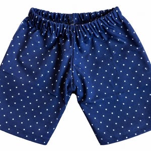 May include: Dark blue shorts featuring a white polka dot pattern throughout the fabric. The shorts have an elasticized waistband with gathered fabric detail and a straight-cut leg design that reaches mid-thigh length with simple hemmed edges.