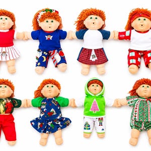 May include: Eight dolls with orange yarn hair and round faces, each wearing different festive outfits including dresses, shirts, trousers, and a hooded sweatshirt with various holiday-themed patterns like Christmas trees, presents, and seasonal colours.