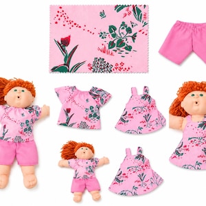 May include: Two dolls with orange yarn hair and green eyes, one wearing a pink floral top and shorts, the other a pink floral dress. Includes a matching pink floral fabric square, a pair of pink shorts, a floral top, and two floral dresses.
