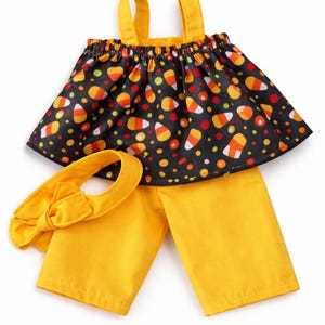 May include: A two-piece outfit consisting of a sleeveless top and matching pants. The top features a black background with a candy corn and polka dot pattern. The pants are solid yellow. A yellow headband with a bow is included in the set.