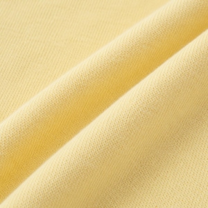May include: Close-up of a pale yellow fabric with visible texture and folds. The material appears to be a soft knit or woven textile, with a subtle sheen. The image highlights the fabric's texture and color.