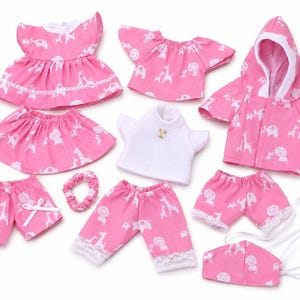 May include: A collection of doll clothing including a pink dress with white animal print, a pink top, a pink hooded jacket, a white shirt, a pink skirt, pink shorts with white bows, pink pants with lace trim, a pink scrunchie, and a pink face mask.
