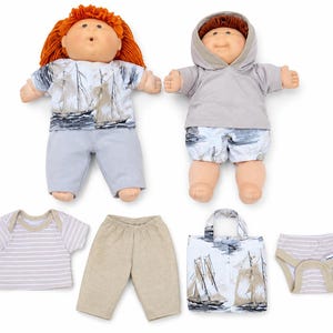 May include: Two dolls with yarn hair, one with orange hair and one with brown hair, wearing outfits with sailboat prints and a grey hoodie. Included are extra clothing items: a striped shirt, beige trousers, a sailboat print shirt, and striped briefs.