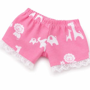 May include: Pink shorts featuring a white animal print pattern of lions, elephants, and giraffes. The shorts have an elastic waistband and white lace trim along the bottom edges of the leg openings, providing a decorative finish to the garment.