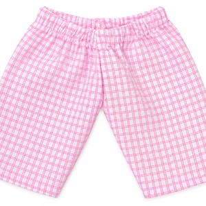 May include: A pair of shorts featuring a pink and white checkered pattern. The garment has an elasticized waistband with a gathered texture, straight-cut legs, and a simple hemline, presenting a classic design with a consistent grid motif.