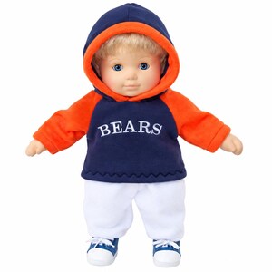 May include: A doll with blonde hair and blue eyes wearing a navy blue and orange hooded sweatshirt with the word BEARS printed in white across the chest, paired with plain white pants and blue and white sneakers with white laces.