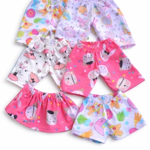 May include: A collection of colorful doll clothes, including shorts and a skirt. The shorts feature various patterns with bunnies, cats, and other whimsical designs. The color palette includes pink, white, and pastel shades, creating a playful and cheerful aesthetic.