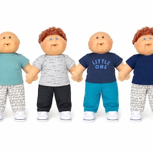 May include: Four dolls with round faces and soft bodies. The first wears a teal shirt and patterned pants. The second has red hair, a grey patterned shirt, and black pants. The third wears a navy shirt with "LITTLE ONE" text and teal pants. The fourth has red hair, a navy shirt, and patterned pants.