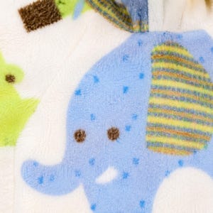 May include: Close-up of a soft, white baby blanket with a blue elephant design. The elephant has a yellow and brown striped ear and is decorated with blue dots. Green and brown shapes are also visible.