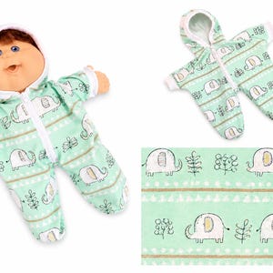 May include: A doll with brown hair and blue eyes wearing a mint green hooded sleeper with a white zipper and a repeating pattern of white elephants and small plants. A matching empty hooded sleeper and a fabric swatch are also displayed.
