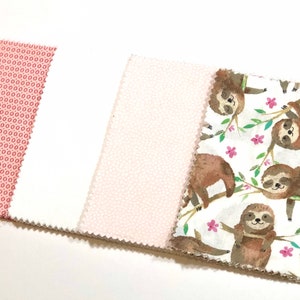 May include: Five fabric swatches, including a solid pink, a pink with a white polka dot pattern, a white fabric with a pink polka dot pattern, a solid white fabric, and a white fabric with a brown sloth pattern.