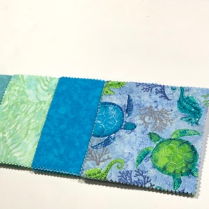 May include: A set of five fabric squares featuring a sea life theme. The squares are in shades of blue, green, and white. One square features a repeating pattern of sea turtles and seahorses. Another square features a repeating pattern of seaweed. The remaining squares are solid blue.