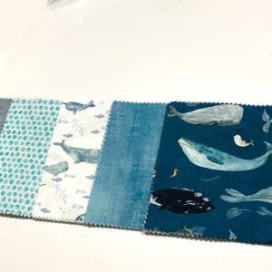 May include: A collection of six fabric swatches featuring a nautical theme. The swatches include a teal blue polka dot pattern, a white fabric with a gray whale and narwhal print, a solid blue fabric, and a teal blue fabric with a gray whale, a black whale, and a seahorse print.