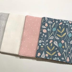 May include: A collection of fabric swatches in various patterns and colors. The swatches include a gray textured fabric, a white fabric, a pink fabric with white polka dots, and a blue fabric with a floral design. The edges of the fabric are serged.