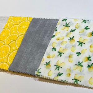 May include: Four fabric squares, one white with a subtle texture, one gray with a subtle texture, and two with a yellow lemon print on a white background.