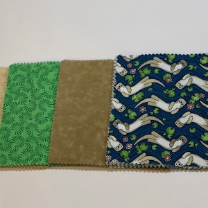 May include: Four fabric squares, one with a green and white floral pattern, one with a brown speckled pattern, one with a beige speckled pattern, and one with a blue background with a white otter pattern.