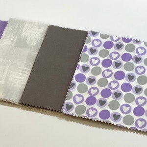 May include: Four fabric squares in a row. The first square is a light gray with a subtle texture. The second square is a dark gray. The third square is white with purple and gray polka dots and white hearts.