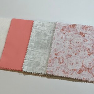 May include: A collection of four fabric squares in various patterns and colors. The first is white with a subtle design, followed by a solid coral square, a gray textured square, and a square covered in a rose pattern.