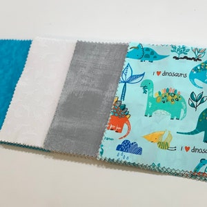 May include: Four fabric squares, one turquoise blue with a marbled pattern, one white with a subtle pattern, one gray with a subtle pattern, and one light blue with a repeating pattern of dinosaurs and the text "I love dinosaurs".