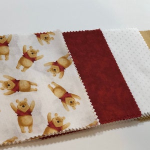 May include: Four fabric squares, one with a white background and a repeating pattern of Winnie the Pooh bears, one burgundy, one white with small white dots, and one beige.