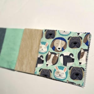 May include: A fabric swatch featuring a dog-themed pattern with various dog breeds on a light teal background. The swatch is accompanied by three solid color swatches: dark teal, light teal, and tan.