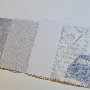 May include: Four fabric swatches in shades of white and gray. The swatches feature different patterns, including a floral design, a small dot pattern, and a solid white fabric. The fourth swatch features a white background with a silver car and the text "Just Married" in silver lettering.