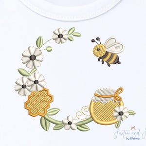 May include: Embroidered design featuring a bee, flowers, and a honey pot. The bee is yellow and black, with white wings. The flowers are white with black centers. The honey pot is gold with a white and gold lid. The design is on a white background.