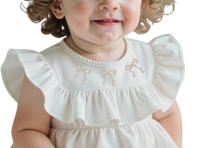 May include: A white baby dress with a ruffled neckline and three embroidered bows. The dress has short sleeves and a gathered skirt.
