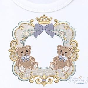 May include: Embroidered design featuring two teddy bears with blue bows, within a decorative frame. The frame includes a crown, bow, and ornate detailing in gold, light blue, and tan colours. The design is on a white background.